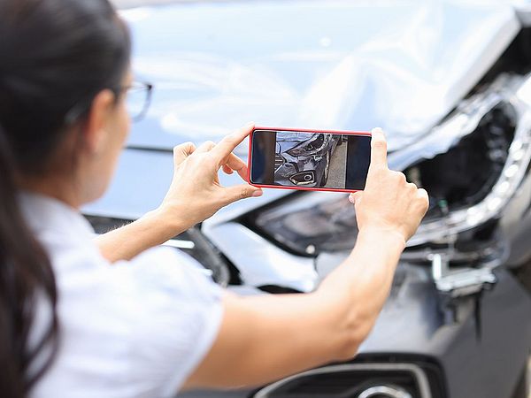 Eine Frau macht mir ihrem Smartphone ein Foto vom entstandenen Schaden an ihrem Auto.