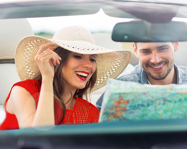 Ein junges glückliches Paar sitzt im Auto und liest eine Landkarte.